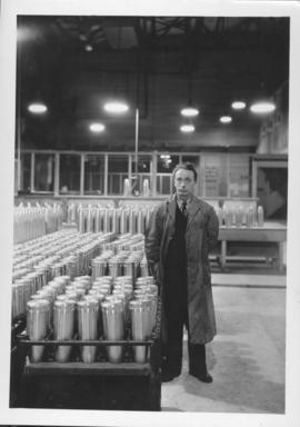 Man standing beside shell cases at Dominion Bridge Company