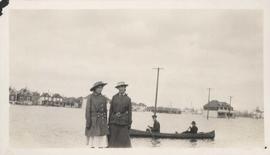 Women standing on flooded residential street with men in canoe, 1916 Flood, Norwood